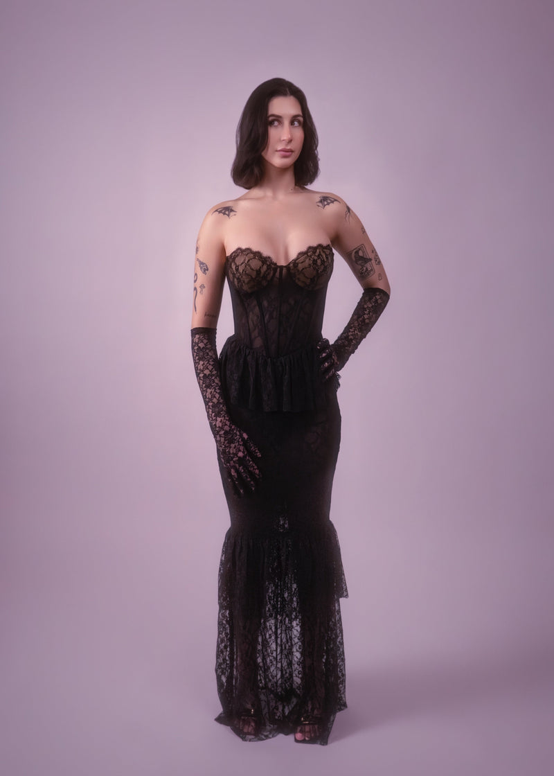 Woman wearing a black lace dress and gloves against a light purple background