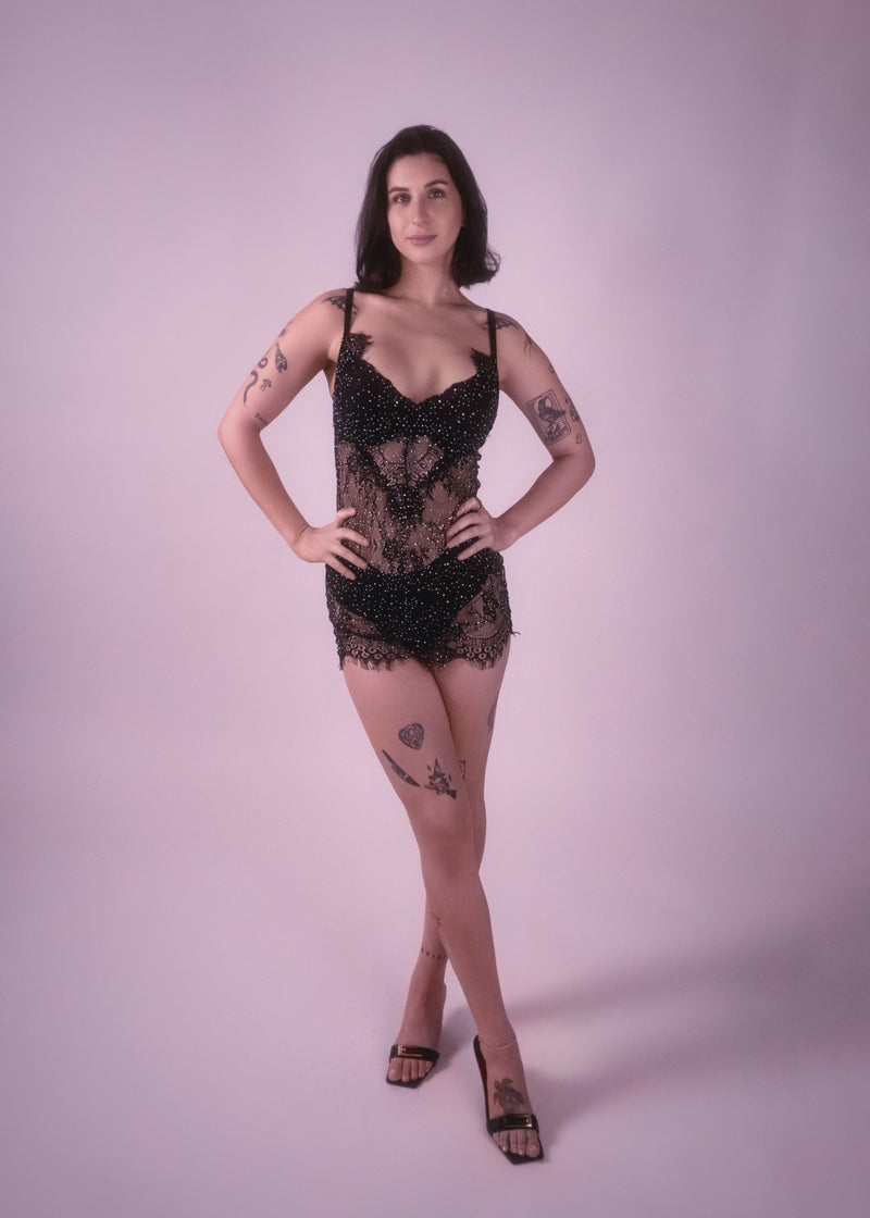 Woman wearing a black lace rhinestone lingerie mini dress on a plain background