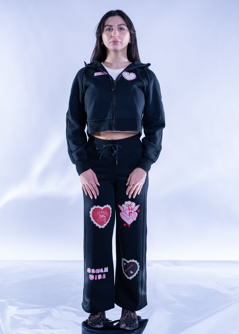 Person wearing a black hoodie and pants with heart designs on a white background