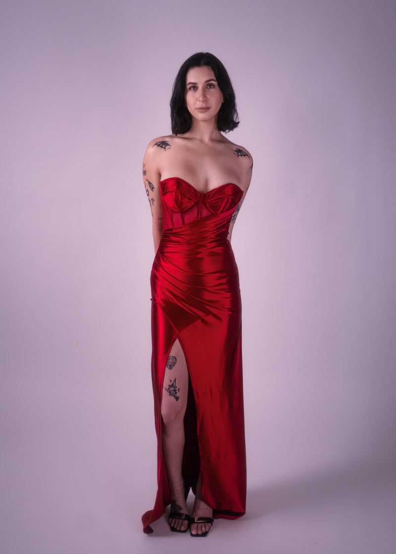 Woman wearing a red strapless satin gown with a slit on a plain background