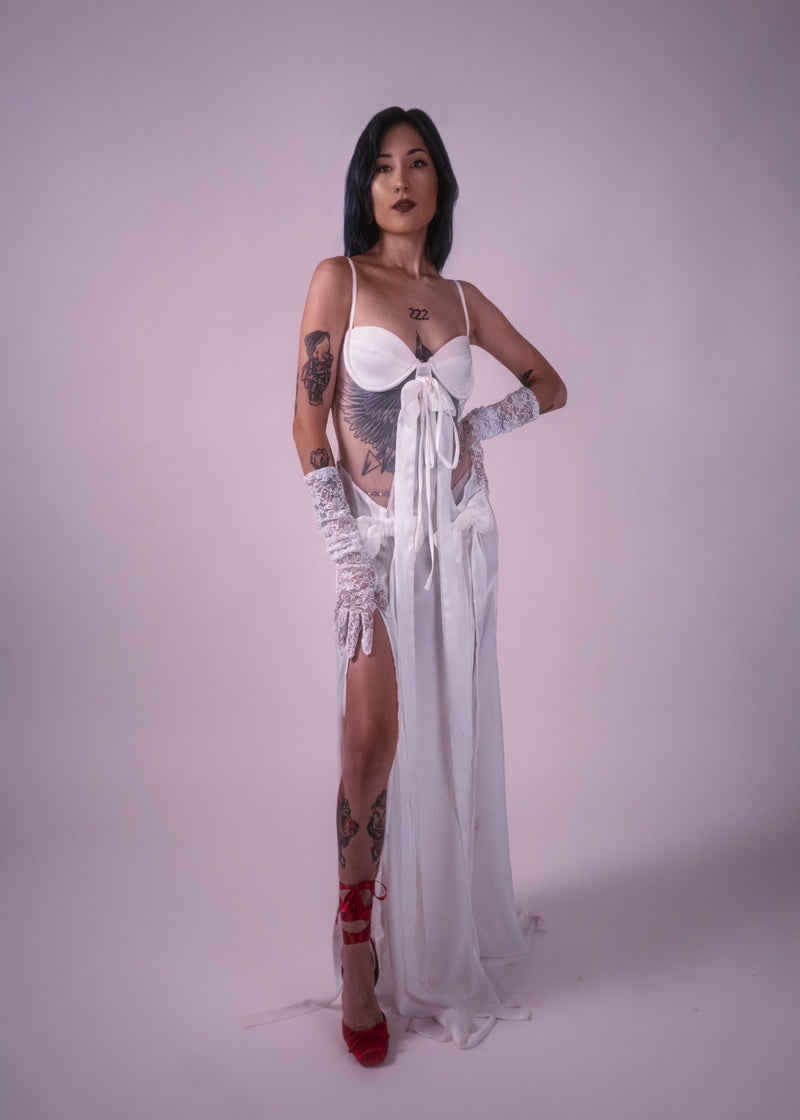 Woman wearing a white lace gown with slits and red shoes on a plain background