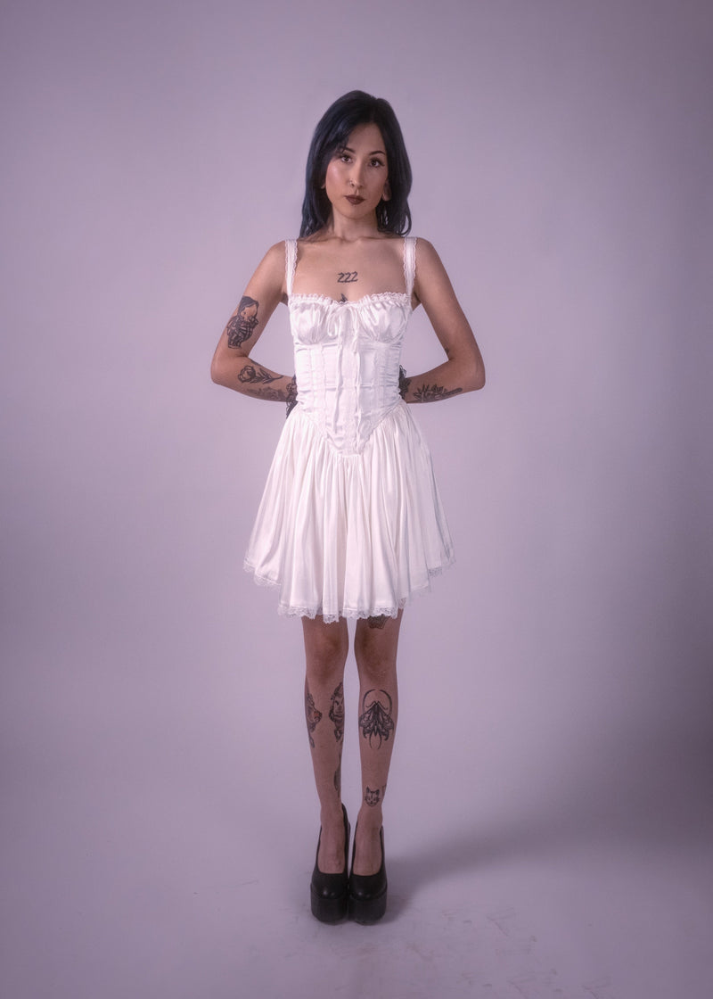 Woman wearing a white corset dress against a plain background